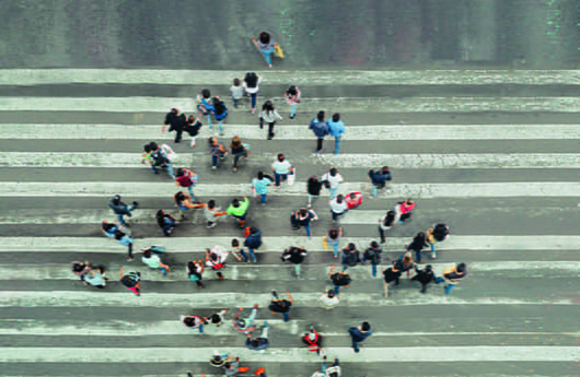 An overhead view of a group of people walking down the road. The group forms the shape of an arrow.