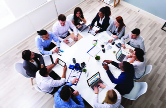 A diverse group of professionals sit around a conference table in a modern office space.