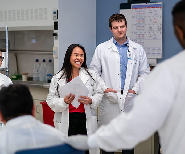 A young female laboratory medicine professional smiles as she addresses a group of her colleagues. Image credit: Greg Gibson
