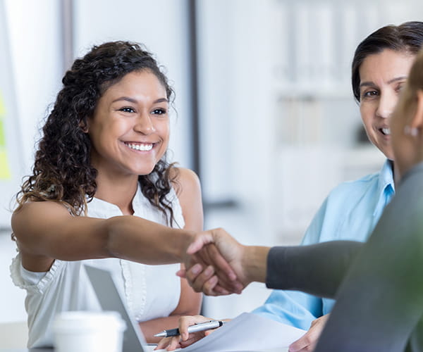 A smiling woman shaking hands with another person.