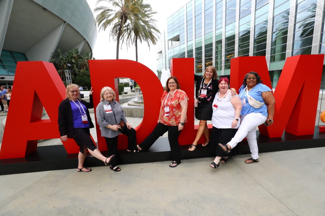 Group of people leaning against and standing in front of large, red ADLM sign