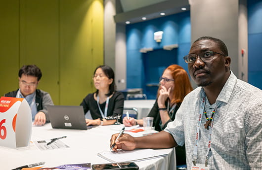 A group of people sitting at a roundtable and taking notes while listening to a presentation.