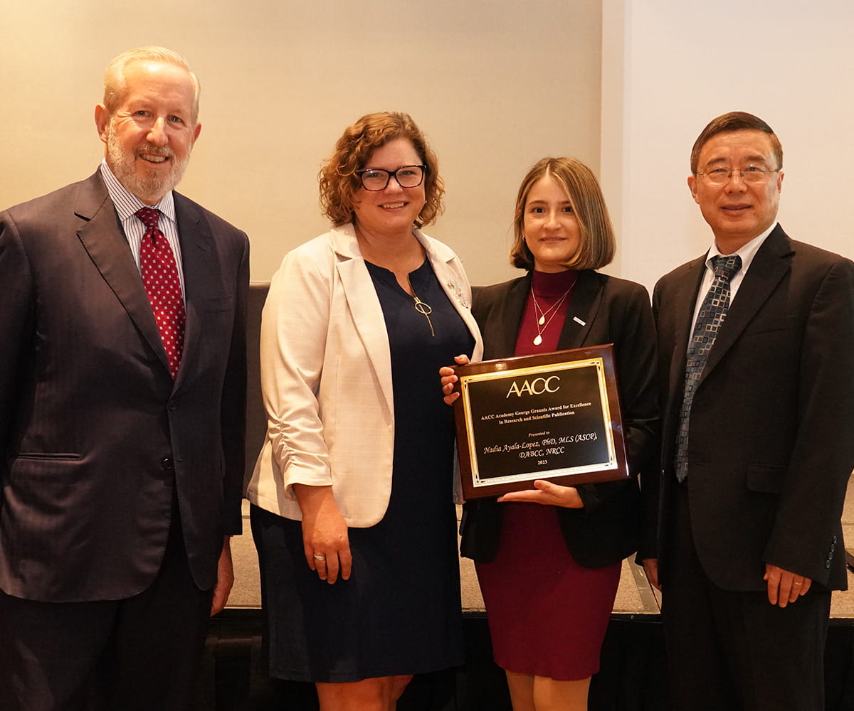 Group of people in business attire posing for picture with one woman holding a plaque