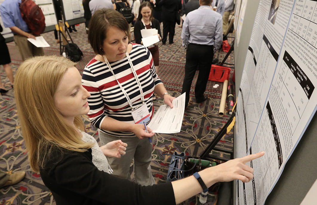 Two women standing in front of a scientific poster and pointing to it.