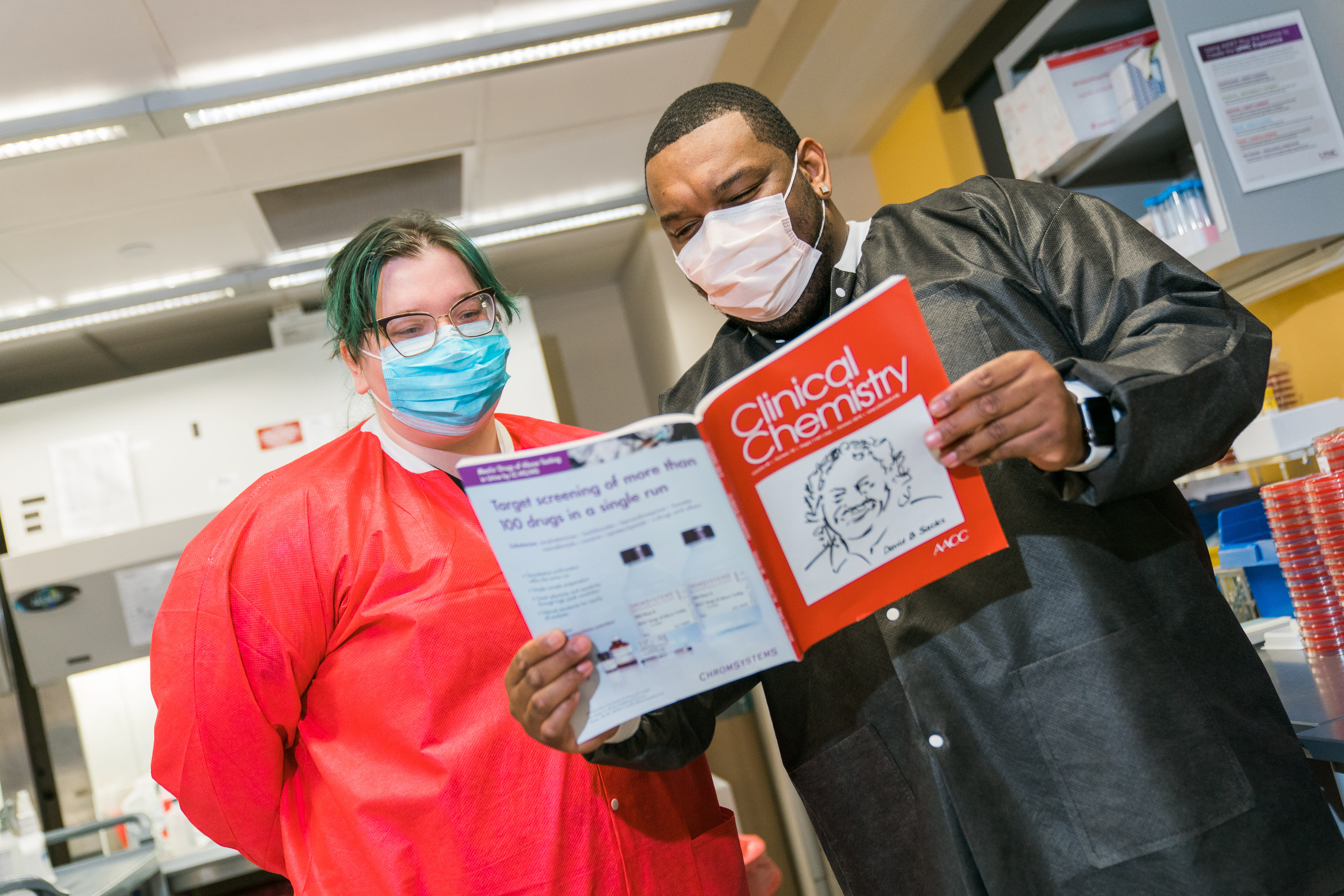 A man and woman in masks reading Clinical Chemistry Journal
