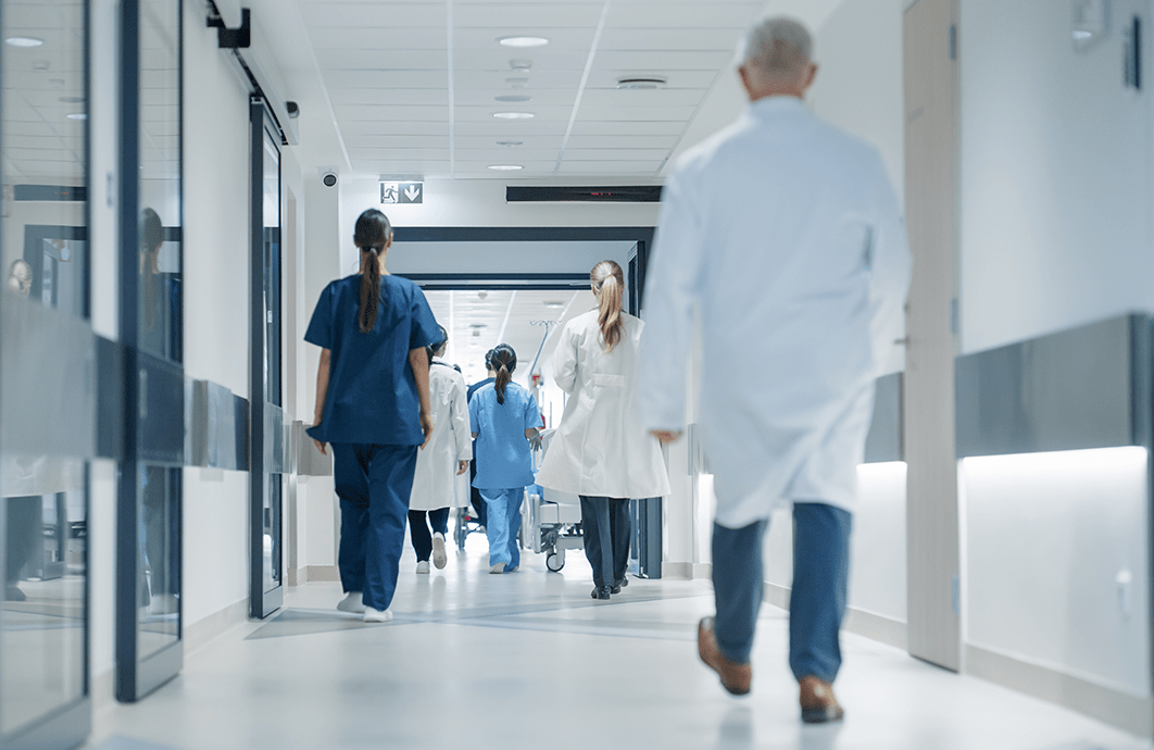 People in lab coats and scrubs walk down the hallway of a hospital.