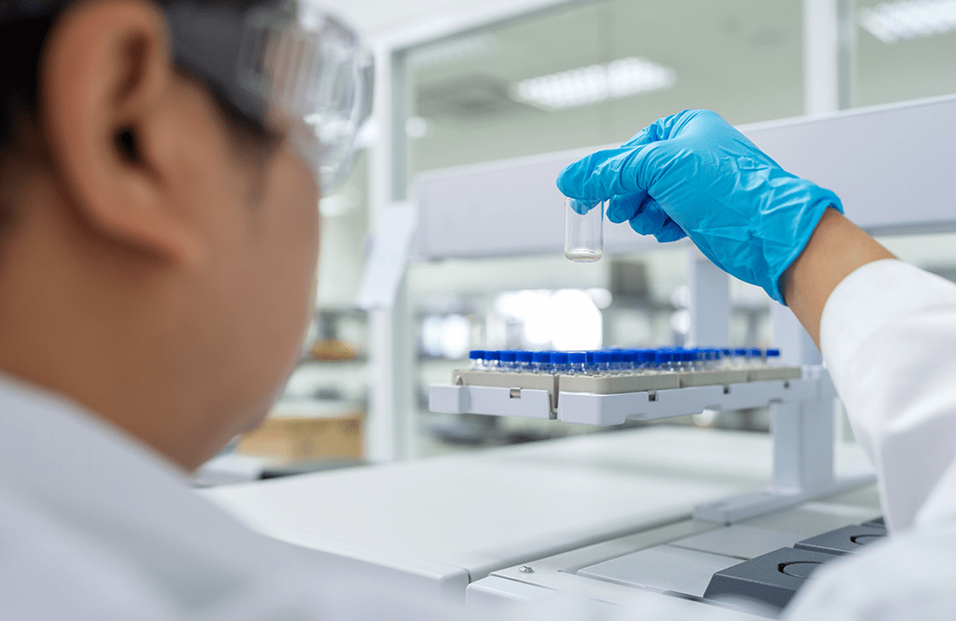 A laboratorian wearing goggles and gloves hold a tube above a tray.