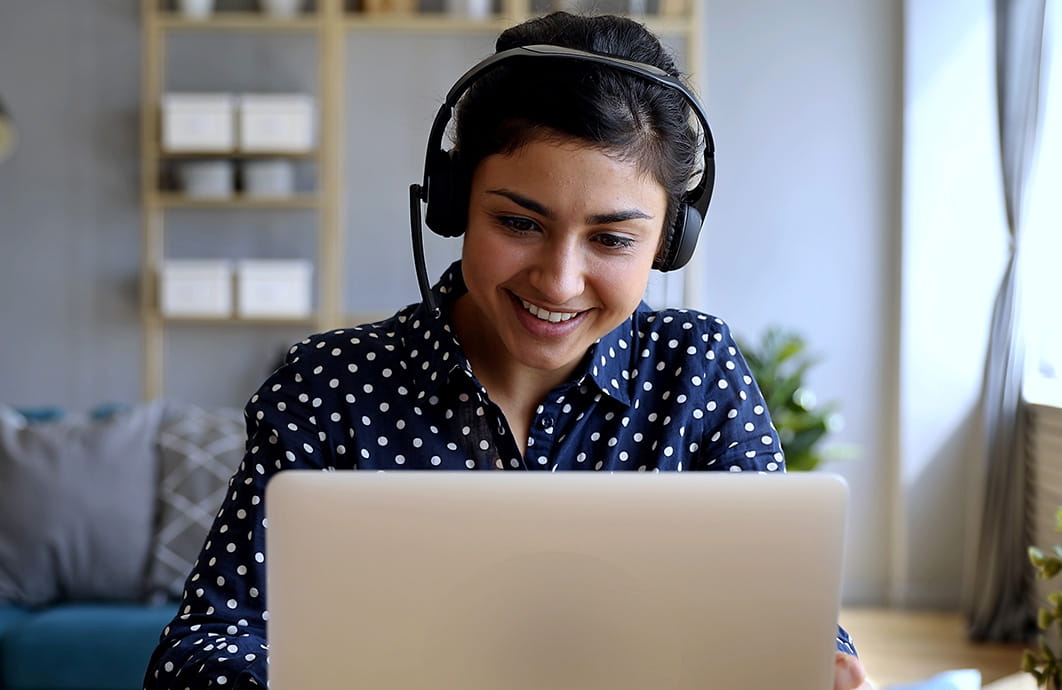A woman wearing headphones smiles while she looks at a laptop.